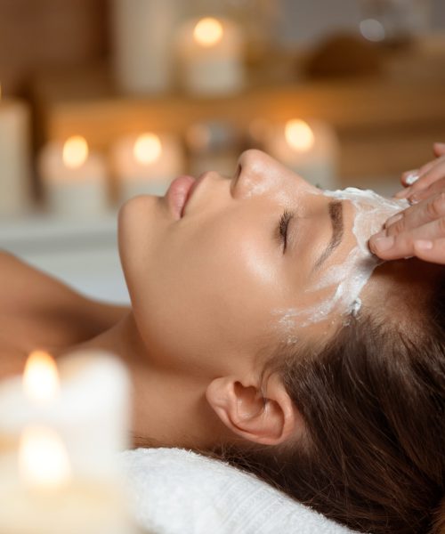 Young beautiful brunette girl in mask for face relaxing in spa salon. Eyes closed. Copy space.