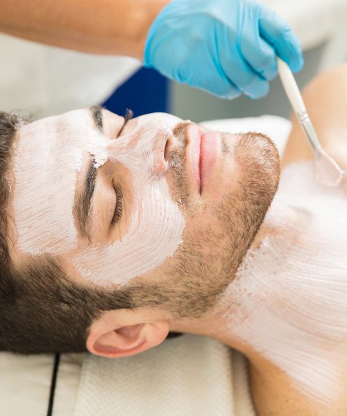 Portrait of an attractive Hispanic young man getting a facial and an anti-aging mask in a health spa